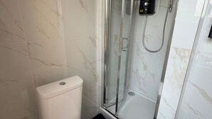 Un bagno con il water, una doccia con porta in vetro e pareti in marmo.