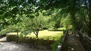 Eine Holzbrücke über einem Bach, umgeben von üppigem Grün und einem gepflegten Rasen.