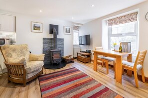 A cozy living room with a fireplace, a sofa, a dining table, and a TV. - 1 Bed in Ambleside (oc-lr108) (Ambleside)