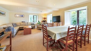 A living room with a sofa, a coffee table, a dining table with chairs, a TV, and large windows. - 4 Bed in Ambleside (oc-lr109) (Ambleside)