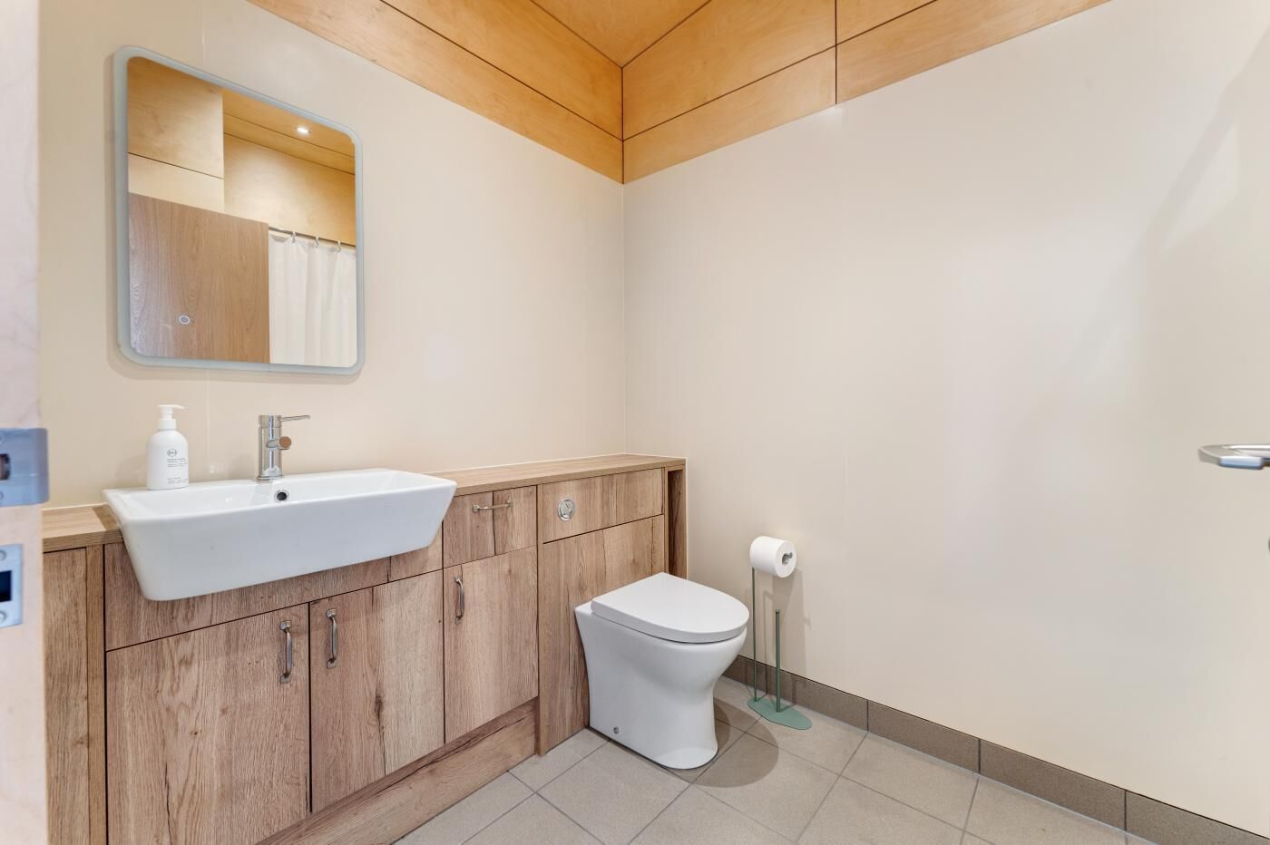 Une salle de bain avec un meuble-lavabo en bois, un lavabo blanc, des toilettes et un miroir.