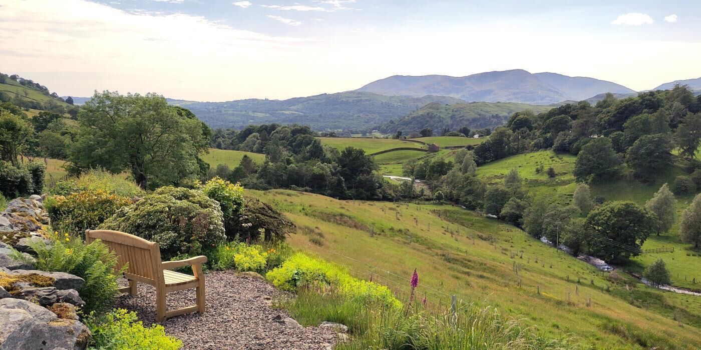 A bench in a rural landscape with rolling hills and a distant mountain range.