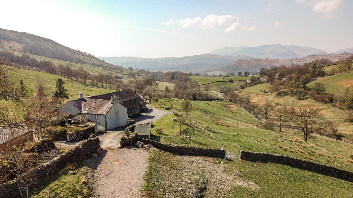 A rural landscape with a stone wall, a building with a sloped roof, and rolling hills in the background.