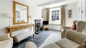 A living room with a fireplace, a television, a sofa, a bench, and a large window with curtains. - 3 Bed in Ambleside (oc-lr121) (Ambleside)