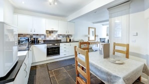 A modern kitchen with white cabinets, a built-in oven, and a dining area with a table and chairs. - 3 Bed in Ambleside (oc-lr121) (Ambleside)