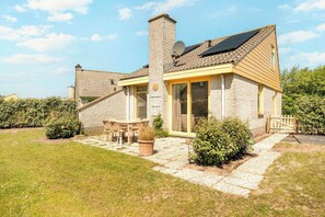 A house with a stone facade, a chimney, a solar panel, a patio with a table and chairs, and a garden. - Detached Beautiful Holiday Home in Julianadorp (Julianadorp)