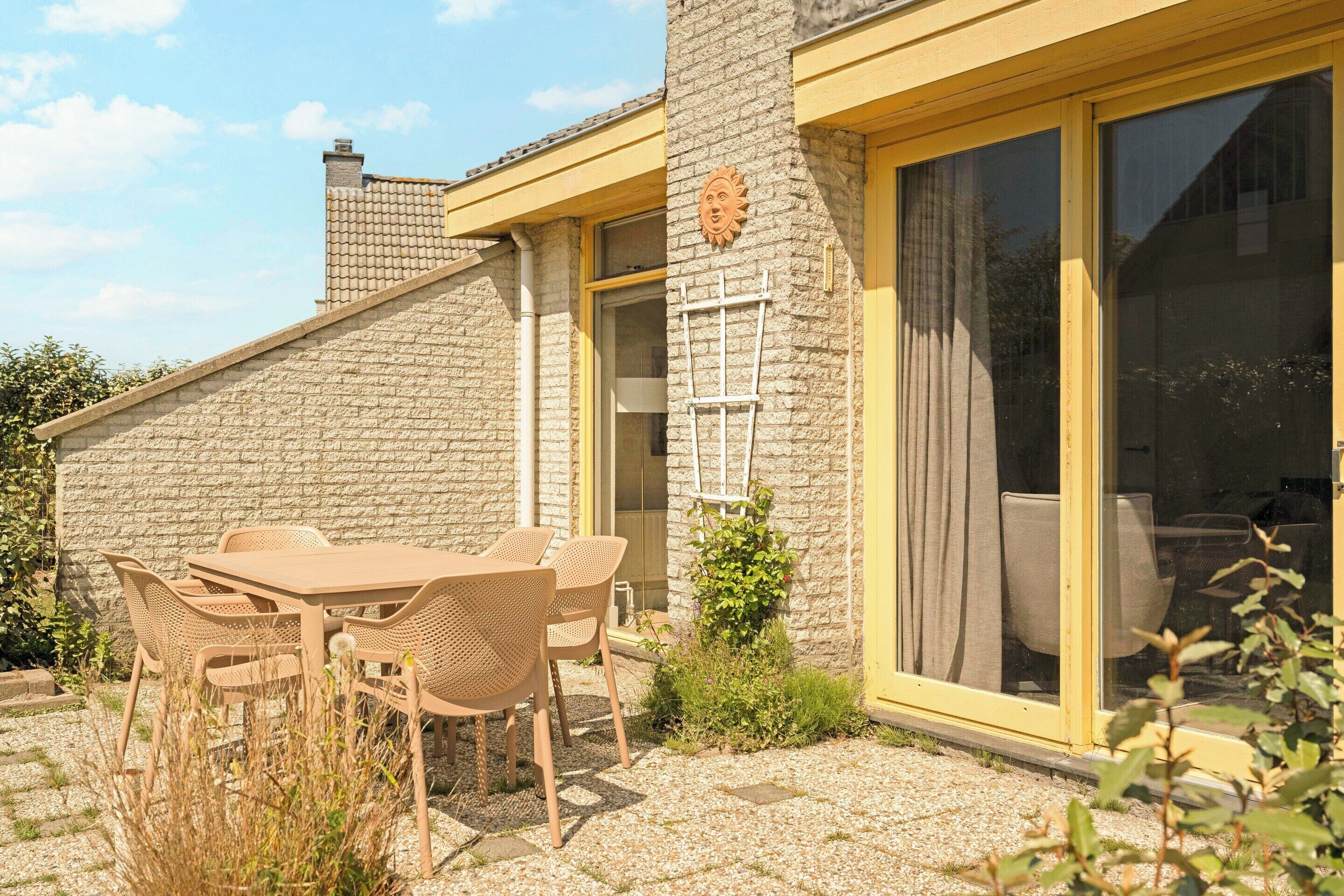 Een terras met een tafel, stoelen, een stenen muur en een schuifpui.