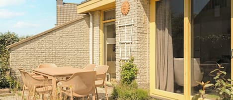 A patio with a table and chairs, a stone wall, and a sliding glass door.