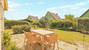 Un patio con tavolo e sedie, circondato da un giardino con siepi e vista su abitazioni.