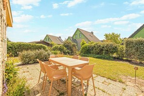 A patio with a table and chairs, surrounded by a garden with hedges and a view of houses. - Detached Beautiful Holiday Home in Julianadorp (Julianadorp)