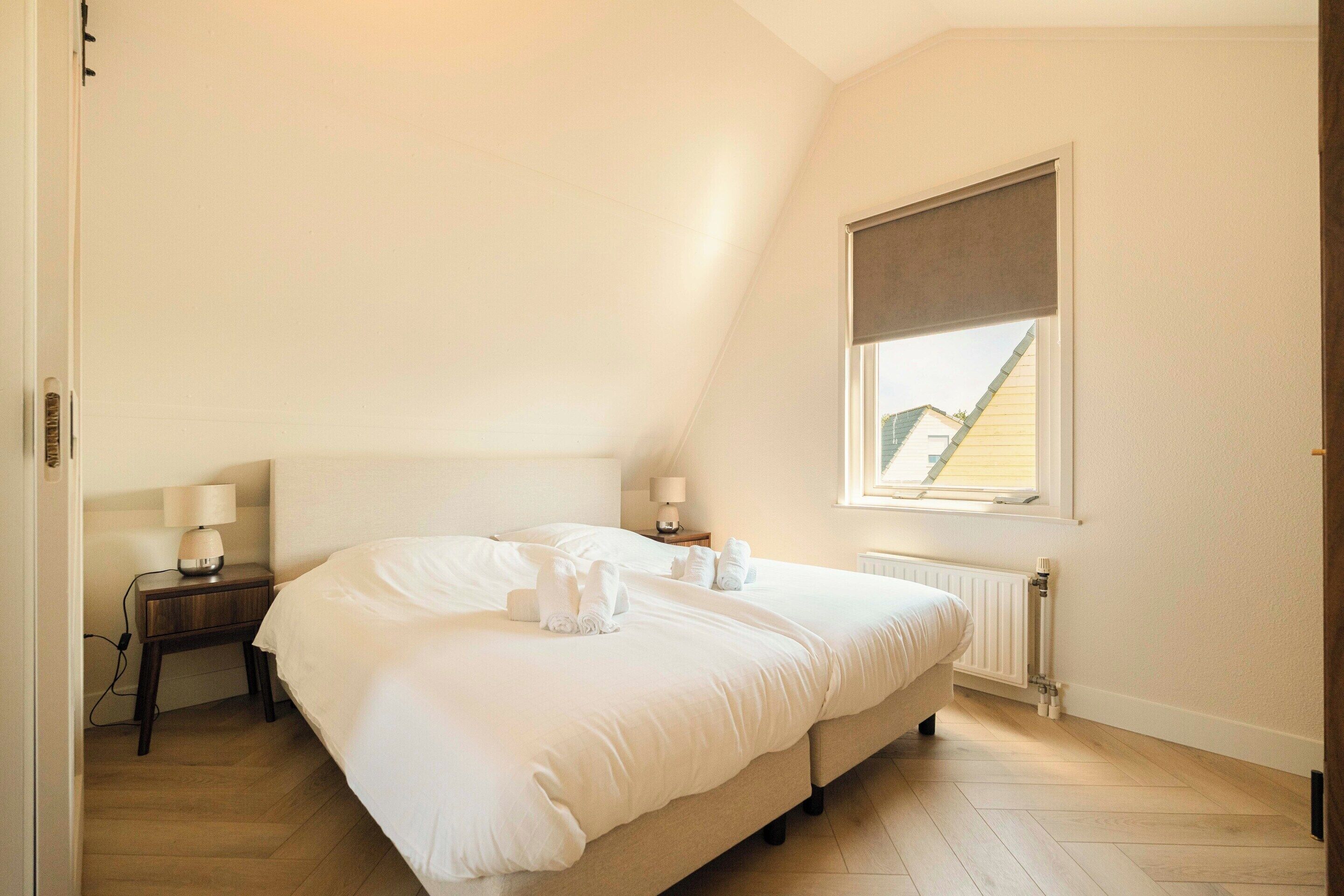Une chambre à coucher avec un lit, des tables de chevet, une fenêtre et un radiateur.