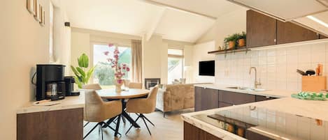A modern kitchen with a dining area, wooden cabinets, a coffee machine, and a TV.