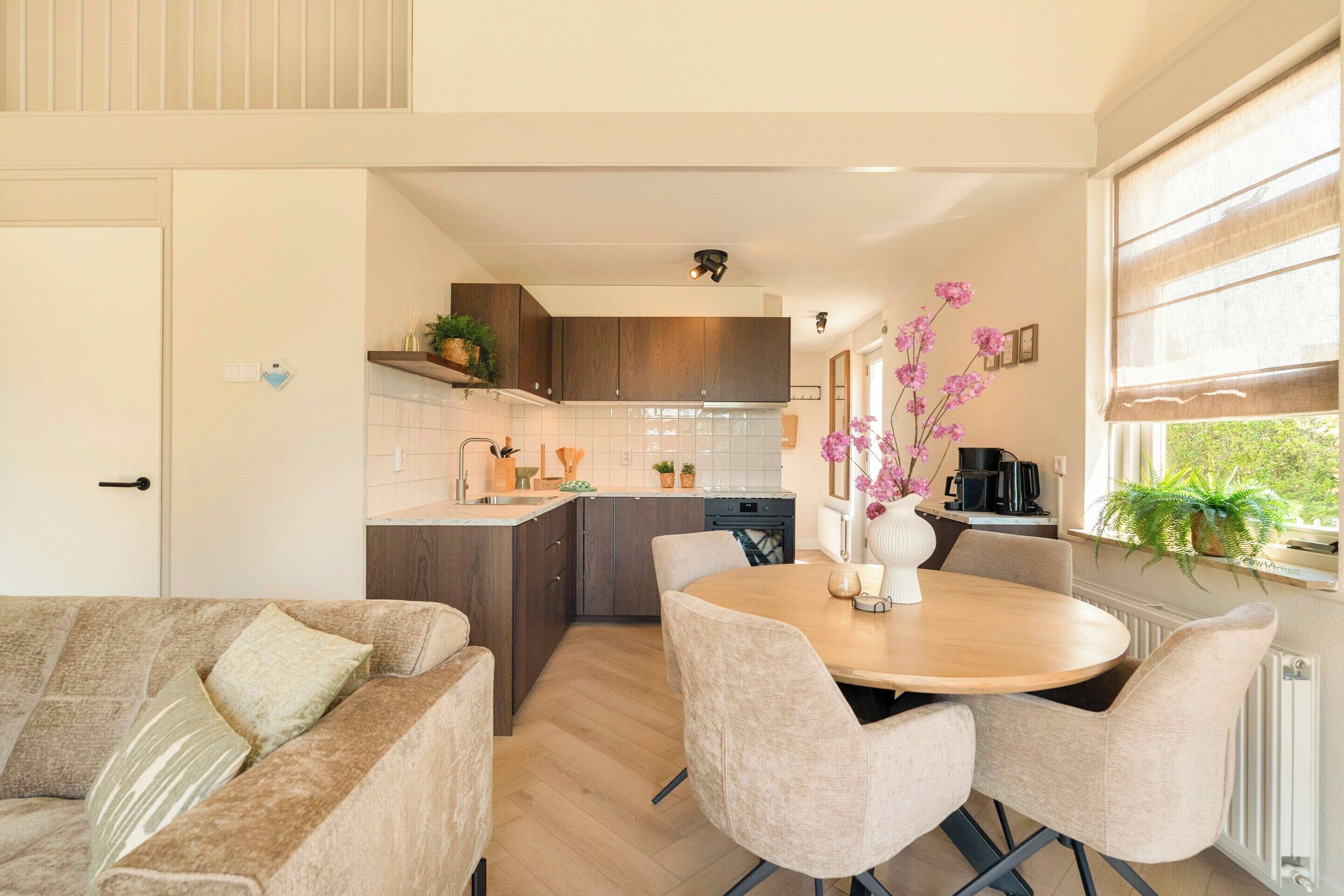 A modern kitchen with a dining area, wooden cabinets, and a window with a view.