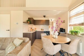 A modern kitchen with a dining area, wooden cabinets, and a window with a view. - Detached Beautiful Holiday Home in Julianadorp (Julianadorp)