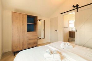 Une chambre avec une armoire en bois, un lit avec du linge de lit blanc et un miroir.