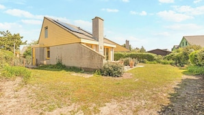 Una casa a un piano con facciata in mattoni, un camino e un piccolo giardino anteriore con prato e vialetto che conduce all'ingresso.