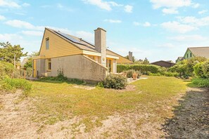 A single-story house with a brick exterior, a chimney, and a small front yard with a lawn and a pathway leading to the entrance. - Detached Beautiful Holiday Home in Julianadorp (Julianadorp)