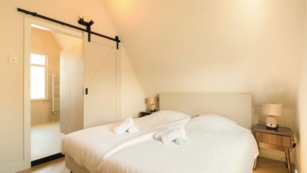 Una camera da letto con un letto, un comodino, una lampada e una porta scorrevole che dà accesso a un bagno.