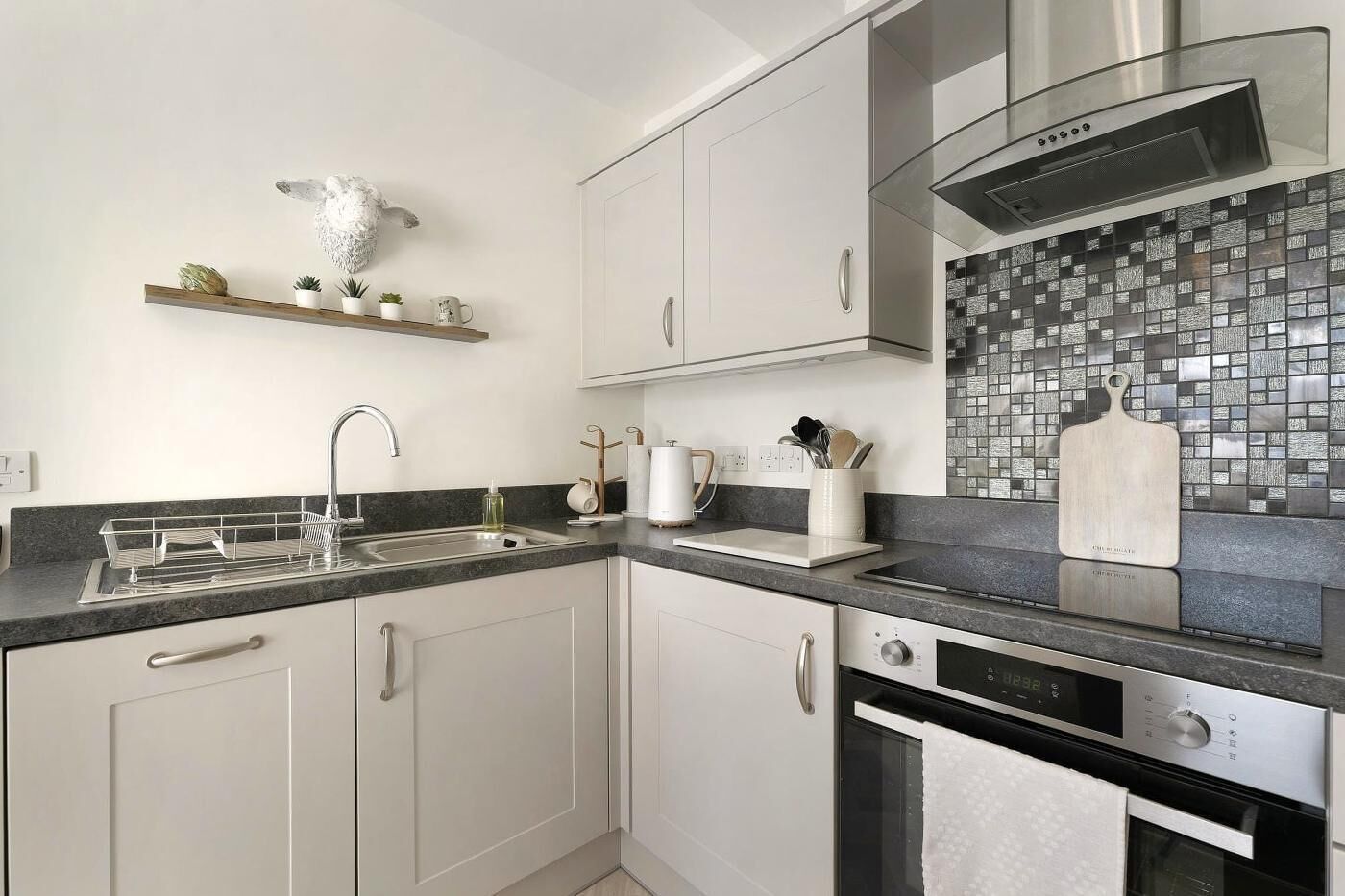 A modern kitchen with white cabinetry, a stainless steel sink, a black countertop, and a tiled backsplash.