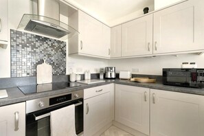 A modern kitchen with white cabinets, a black countertop, a stainless steel range hood, a microwave, and a toaster. - 1 Bed in Portinscale (oc-lr185) (Portinscale)