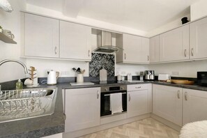 A modern kitchen with white cabinetry, a black countertop, and a herringbone-patterned backsplash. - 1 Bed in Portinscale (oc-lr185) (Portinscale)