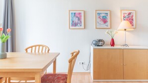 Huoneessa on puinen pöytä, tuoleja, kaappi ja seinälle ripustettuja taideteoksia.