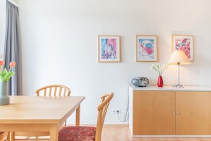 Ein Zimmer mit Holztisch, Stühlen, einem Schrank und Wandbildern.