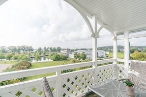 Ein überdachter Balkon mit Blick auf einen See, Gebäude und Grünflächen.