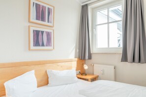 Ein Hotelzimmer mit einem Holzkopfteil, einem Bett mit weißen Leinen, einem Nachttisch mit einer Lampe und zwei gerahmten Bildern an der Wand.