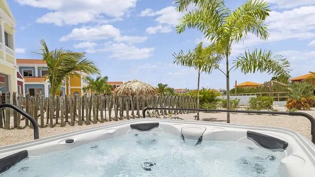 Un jacuzzi con cerramiento de madera, palmeras y edificios al fondo.