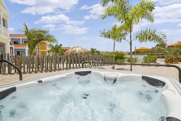 A hot tub with a wooden fence, palm trees, and buildings in the background.
