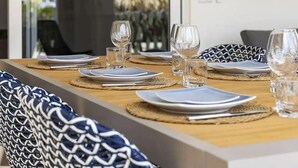 Una mesa de comedor dispuesta con platos, vasos y cubiertos, con cojines estampados en las sillas.