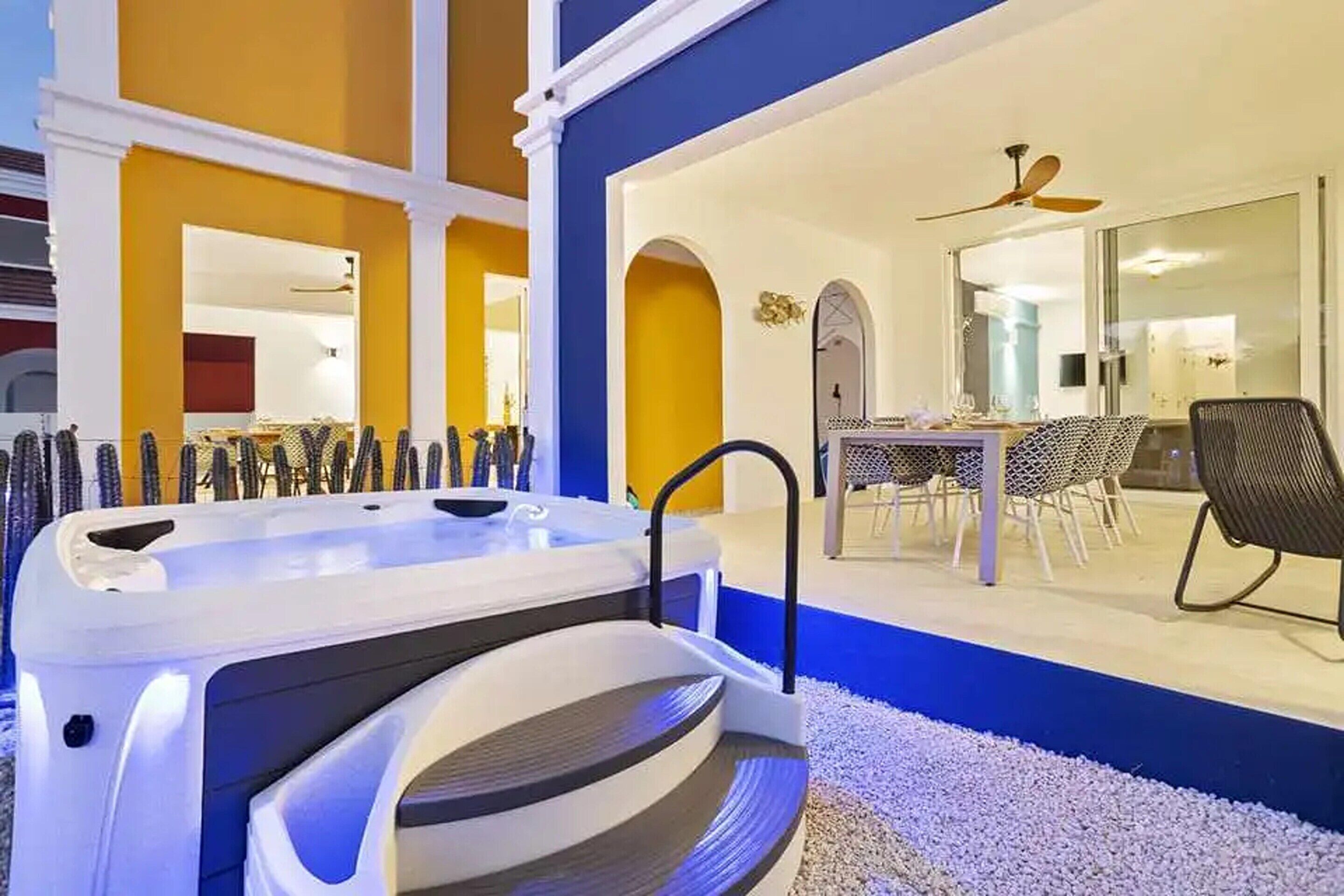 A modern outdoor hot tub area with a dining table and chairs, surrounded by a white gravel area and a blue wall.