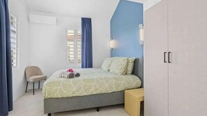 Un dormitorio con cama, una silla, armario y ventana con cortinas.