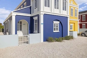 Um edifício de vários andares com fachada azul e branca, um caminho de entrada de cascalho e um portão.