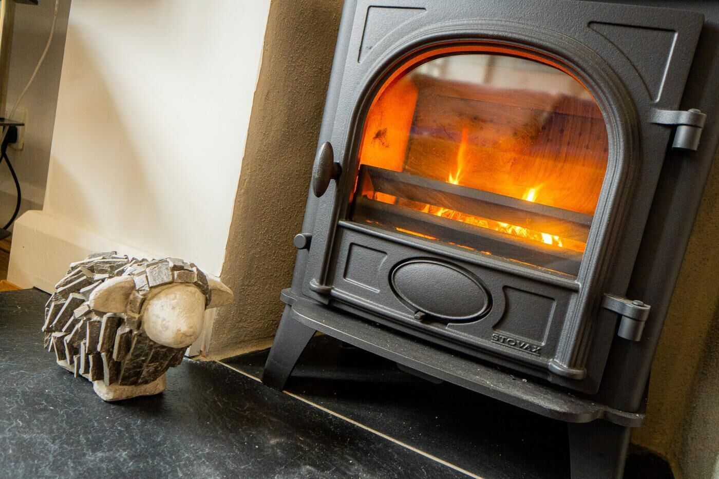 A wood-burning stove with a visible fire, a small decorative item resembling a snowman, and a textured wall.