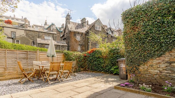 A stone building with a garden patio featuring a table and chairs, a wooden fence, and a stone wall with ivy. - 3 Bed in Ambleside (oc-lr102) (Ambleside)