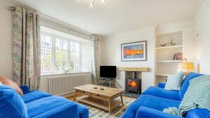 A living room with blue sofas, a wooden coffee table, a TV, a fireplace, and a window with curtains. - 3 Bed in Ambleside (oc-lr102) (Ambleside)