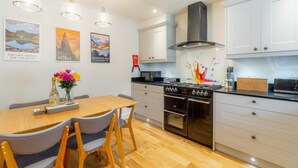 A modern kitchen with a dining area, white cabinetry, stainless steel appliances, and decorative wall art. - 3 Bed in Ambleside (oc-lr102) (Ambleside)