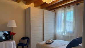 A bedroom with a bed, a chair, a TV, a lamp, and a window with curtains. - Spacious, fully furnished two-room apartment with a terrace and a garage, 20 minutes from Orio Airport (Villongo)