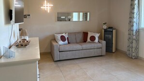 A modern living room with a sofa, a flat-screen TV, a mirror, and a heater. - Spacious, fully furnished two-room apartment with a terrace and a garage, 20 minutes from Orio Airport (Villongo)