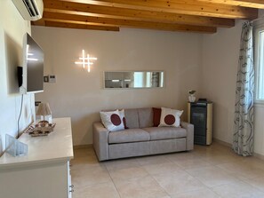 A modern living room with a sofa, a flat-screen TV, a mirror, and a heater. - Spacious, fully furnished two-room apartment with a terrace and a garage, 20 minutes from Orio Airport (Villongo)