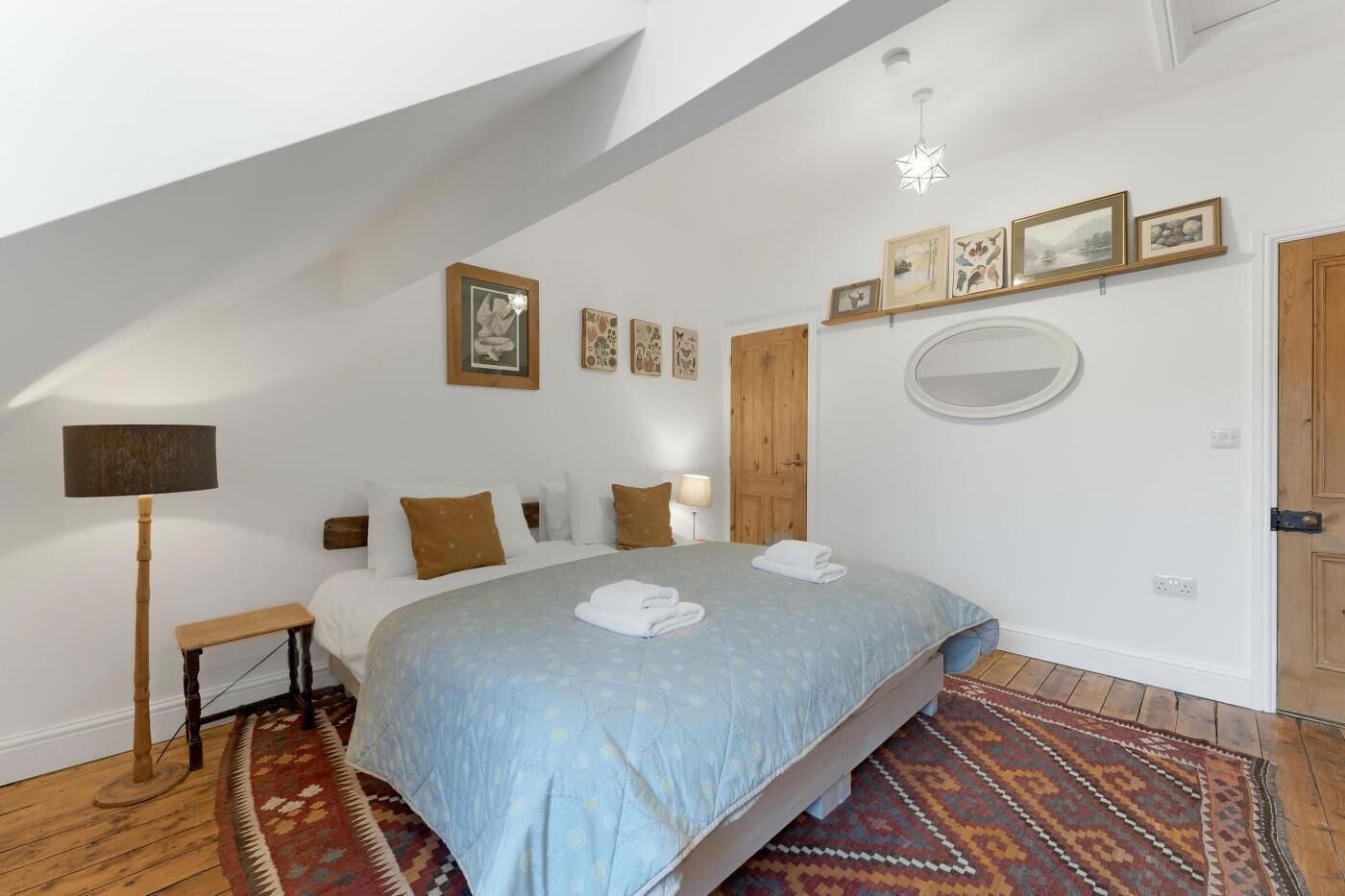 Ein Schlafzimmer mit Bett, Nachttisch, Lampe, Holztür und Wandbildern.