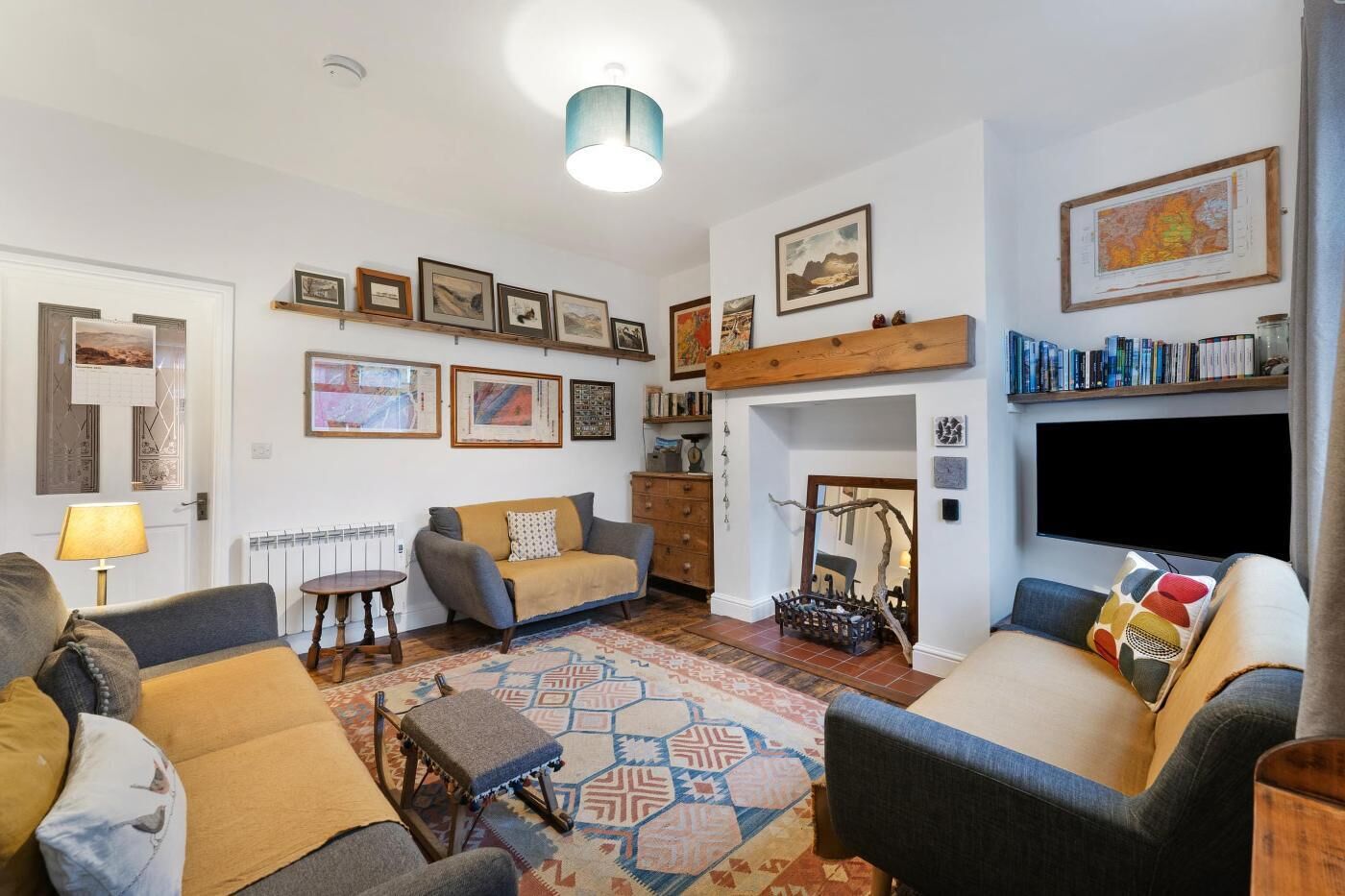 Een woonkamer met een bank, fauteuils, een salontafel, een open haard, een televisie en diverse lijstwerken aan de muren.