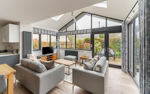 A modern living room with a sofa, coffee table, and TV, large windows, and a view of the outdoors. - 2 Bed in Ambleside (oc-lr145) (Ambleside)