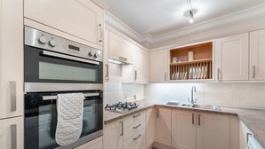 A kitchen with two ovens, a stove, a sink, and a dish rack.