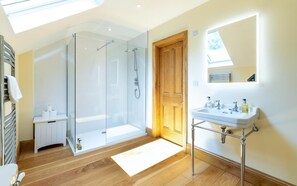 Ein modernes Badezimmer mit Duschkabine aus Glas, einer Holztür, einem weißen Waschbecken mit Chromarmaturen und einem Oberlicht.
