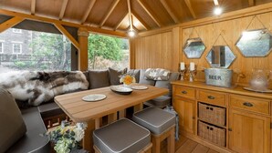 Een gezellig interieur met houten lambrisering, een bank, een eettafel en een kast met honingraatspiegels.