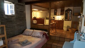 Un dormitorio con cama, una ventana pequeña, kitchenette y un baño con lavamanos y espejo.
