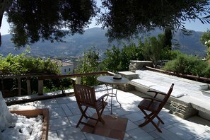 Une terrasse avec deux chaises en bois, une petite table ronde et un banc en pierre.